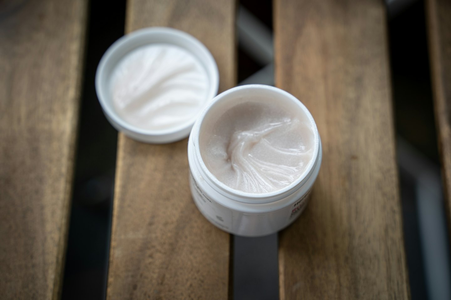 Open jar of white cream on a wooden surface.
